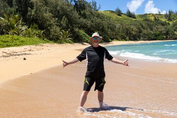 Happy man wearing a floppy hat, sunglasses and a sun shirt for protection from UV rays having fun on a tropical island, beach for summer vacation. 