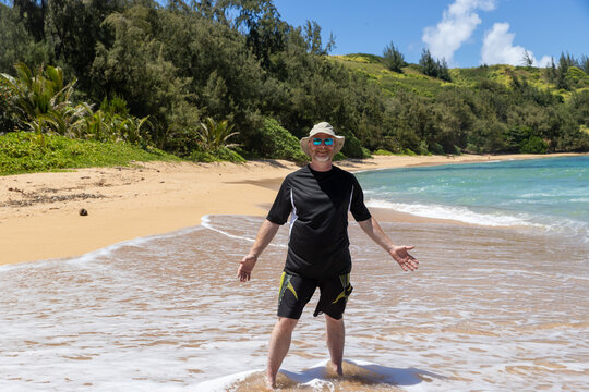 Happy man wearing a floppy hat, sunglasses and a sun shirt for protection from UV rays having fun on a tropical island, beach for summer vacation. 