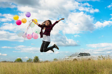 Cheerful beauty woman holding balloons relax sitting under big tree in green park with happiness. Woman Hands holding vibrant air balloons play on birthday party happy time summer on sunshine outdoor