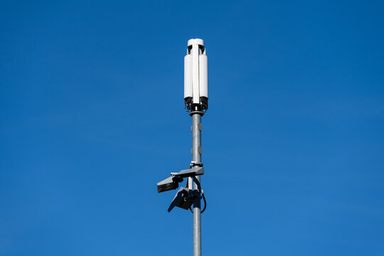 Mobile technology communication cell tower against a sunny blue sky, narrow metal monopole and small white panel antenna
