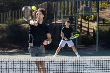 Two adult men playing an intense game of tennis together on an outdoor court. The sport is fast and they are training during practice. 