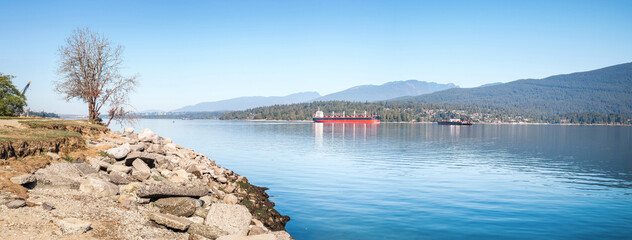 Cargo ship anchored in inlet in front of mountain scene. Summer marine transport panorama. Burrard...