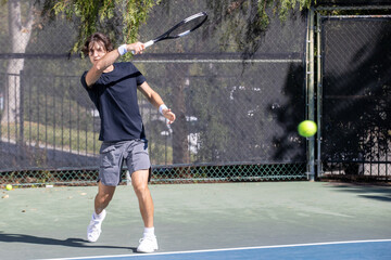 Active tennis player playing a game on an outdoor court. The man is wearing gray shorts and a black tee shirt holding a racquet. 
