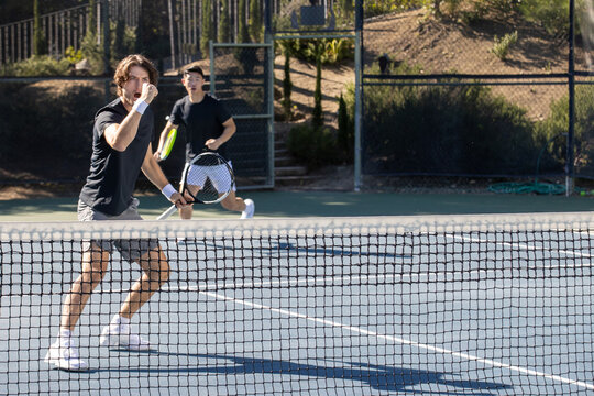 Two adult men playing an intense game of tennis together on an outdoor court. The sport is fast and they are training during practice. 