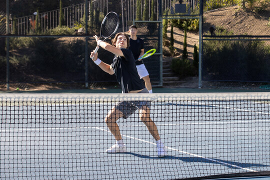 Two adult men playing an intense game of tennis together on an outdoor court. The sport is fast and they are training during practice. 