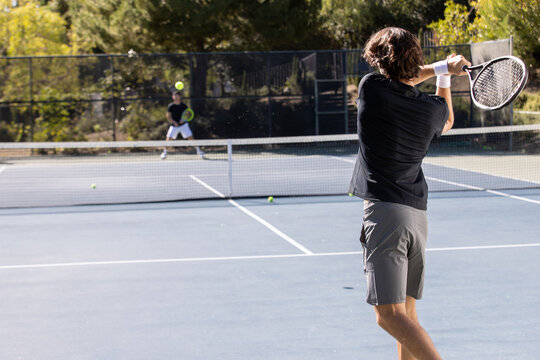 Two adult men playing an intense game of tennis together on an outdoor court. The sport is fast and they are training during practice. 