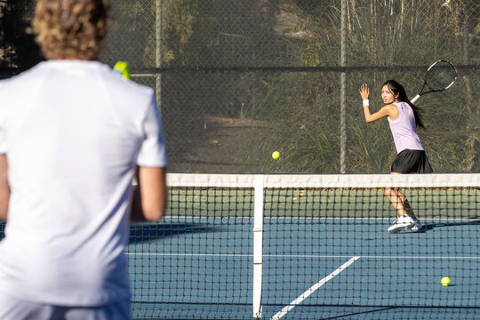 Two tennis players, a man and a woman practice together on the court by hitting the ball over the net. The workout is fun and active. 