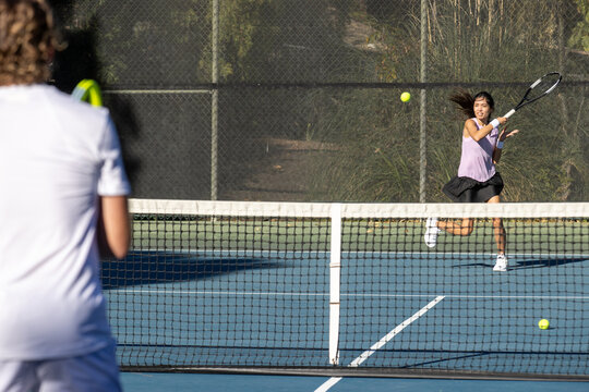 Two tennis players, a man and a woman practice together on the court by hitting the ball over the net. The workout is fun and active. 