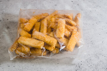 Bag of frozen breaded fish sticks close-up on grey background