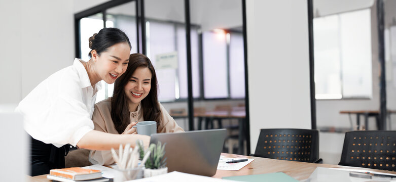Two businesswoman working together on laptop. Creative female executives meeting in an office using laptop pc.