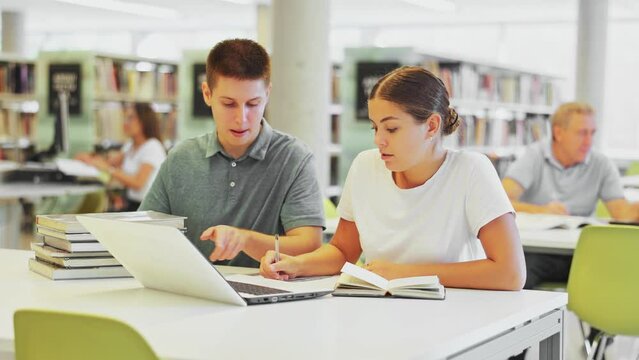 View on a mature man and a young female european student studying together with a laptop in library. High quality 4k footage