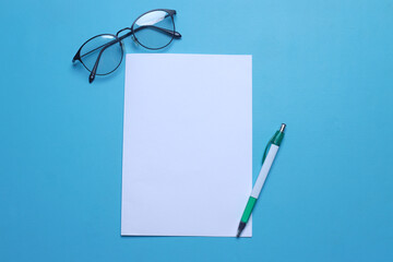 Top view of blank white paper sheet for mockup with pen and glasses on blue background