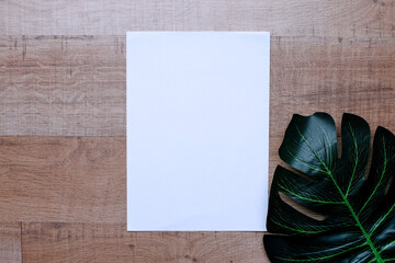 Blank white paper for mockup and monstera leaf on wood background