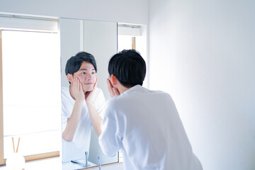 洗面台の鏡の前で肌に触れる男性