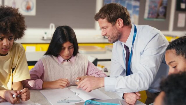 Male secondary or high school teacher helping secondary or high school students to build model of molecule or atom in science class - shot in slow motion