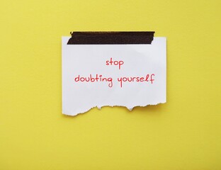 Note on yellow background with handwritten text STOP DOUBTING YOURSELF, concept of self-doubt, lack...