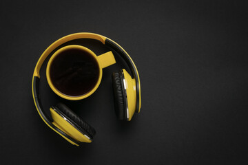 Coffee mug and yellow headphones on a black background. Space for text.