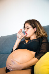 pregnant woman taking care of herself drinking water, sitting on her couch