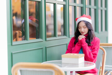 Young Asian woman in Santa hat smiling and holding Christmas gifts smile happily While decorating the Christmas tree at home, the idea of ​​celebrating New Year's Day