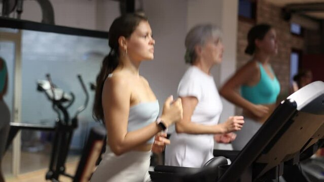 Focused motivated young girl leading healthy active lifestyle doing cardio workout in gym, running on treadmill