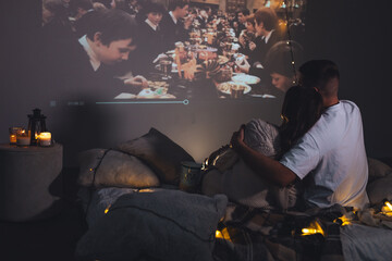 Romantic evening together, calm weekend, slow living. Loving young happy couple having a date at home, watching movies in bed, enjoying each other. Cozy atmosphere, atmospheric lights, leisure