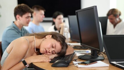 Tired young female employee engaged in programming or data analysis in coworking space dozing off at workplace due to intensive work