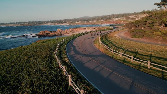 Group of cyclists riding on a curved road at the seaside with scenic view of the sea, aerial tracking shot