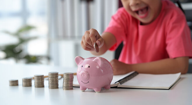Cute little Asian girl playing with coins, making money in piles, putting money in a piggy bank. Count your saved coins and learn about frugality. Educational planning, management, future concepts.
