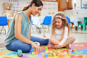 Woman, kid and toys for playing in classroom for learning, fun or development. Female teacher, little girl and colorful blocks for education, growth or milestone in childhood with exciting activity - obrazy, fototapety, plakaty