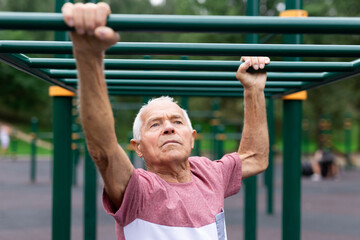 Obraz premium Senior man climbing on horizontal ladder in outdoor workout station