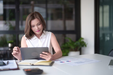Asian businesswomen reading marketing business report to checking financial chart data on digital tablet and writing notes while analyze investment and market stock of new startup in outside office