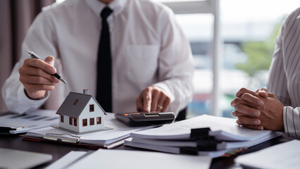 Businessman real estate seller using calculator to calculating and pointing on house model to...