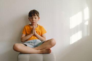 Obraz premium A boy in an orange T-shirt prays at home. Reading the Holy Bible. Concept for faith, spirituality and religion. Peace, hope.