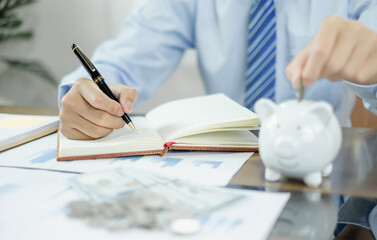 Man calculating her expenses on a notebook putting coin into piggy bank. Saving money with coins Step into a business that is growing to be successful and save for retirement concepts