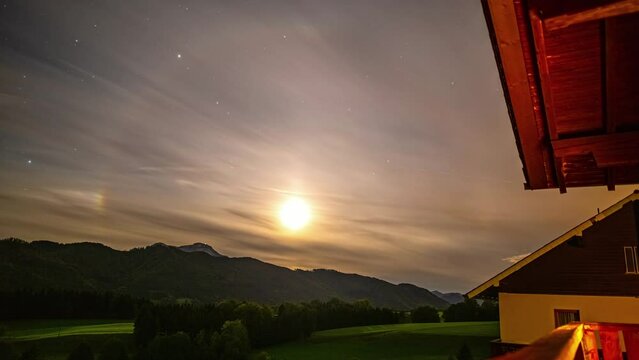 Timelapse during sunset from house in Alps, feint halo around sun, low stratus cloud drifting past.
