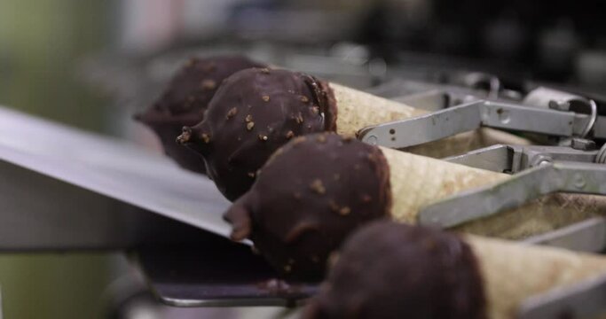 Food industry and technology. Closeup view of a commercial packaging machine wrapping ice cream cones coated in chocolate and peanut in a plastic pack. 