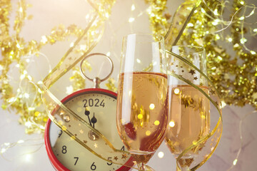 New Year 2024 celebration festive background with champagne glasses and clock over golden bokeh...