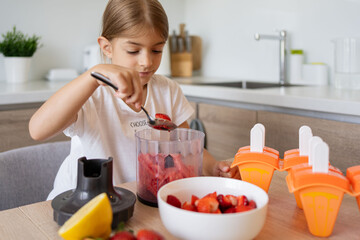 Portrait of cute child girl making ice cream. Kid have fun making with homemade fruit puree ice...