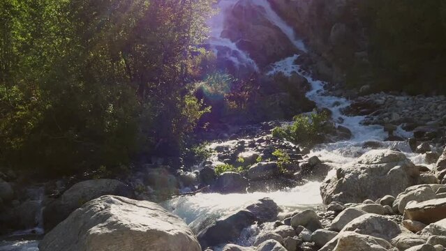 Fast mountain river flows from Alikbek waterfall at sunny day, rapid and furious water splash on rocks outdoor