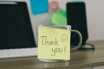 Mug and sticky note with Thank You text on work table.