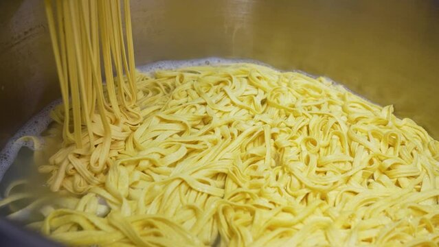 Strands of fresh homemade noodles slowly descend into a big cooking pot