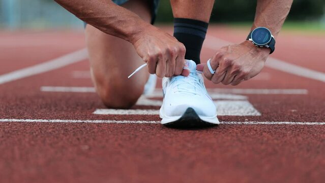 Runner ties his sports shoes to start training on running track, close-up