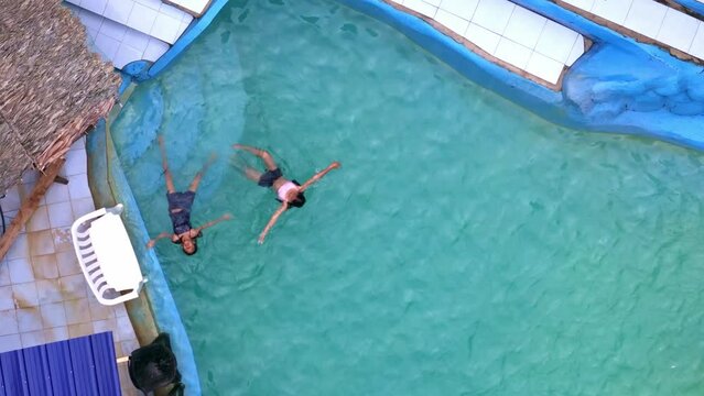 Two young girls swimming on their back in a blue swimming pool. Aerial shot.