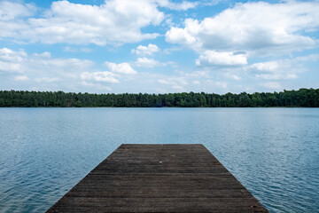 This image presents a tranquil wooden dock leading out to a calm and expansive lake. The simplicity of the composition, with the wooden platform jutting into the water, invites contemplation and a