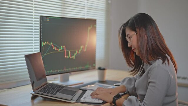 Asian Business Woman is checking Bitcoin or stock market price chart on the digital exchange on a laptop monitor computer, cryptocurrency future price action prediction. Trading Stock Bitcoin ETF.