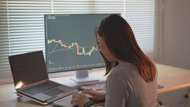 Asian Business Woman is checking Bitcoin or stock market price chart on the digital exchange on a laptop monitor computer, cryptocurrency future price action prediction. Trading Stock Bitcoin ETF.