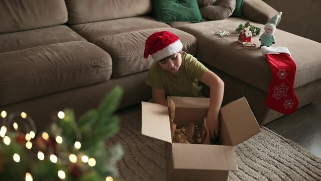Kid boy decorating Christmas tree put off balls from the box authentic real celebration image lifestyle. Xmas with family children fun at cozy home