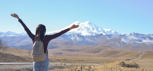 A happy female traveler with a backpack behind her back and her arms raised up admires the...