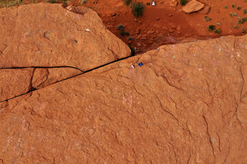 Two boys hike along red rock slab near cliff drone shot