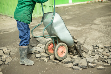 Obraz premium Builder removes broken stone. Man carries cobblestones in cart.